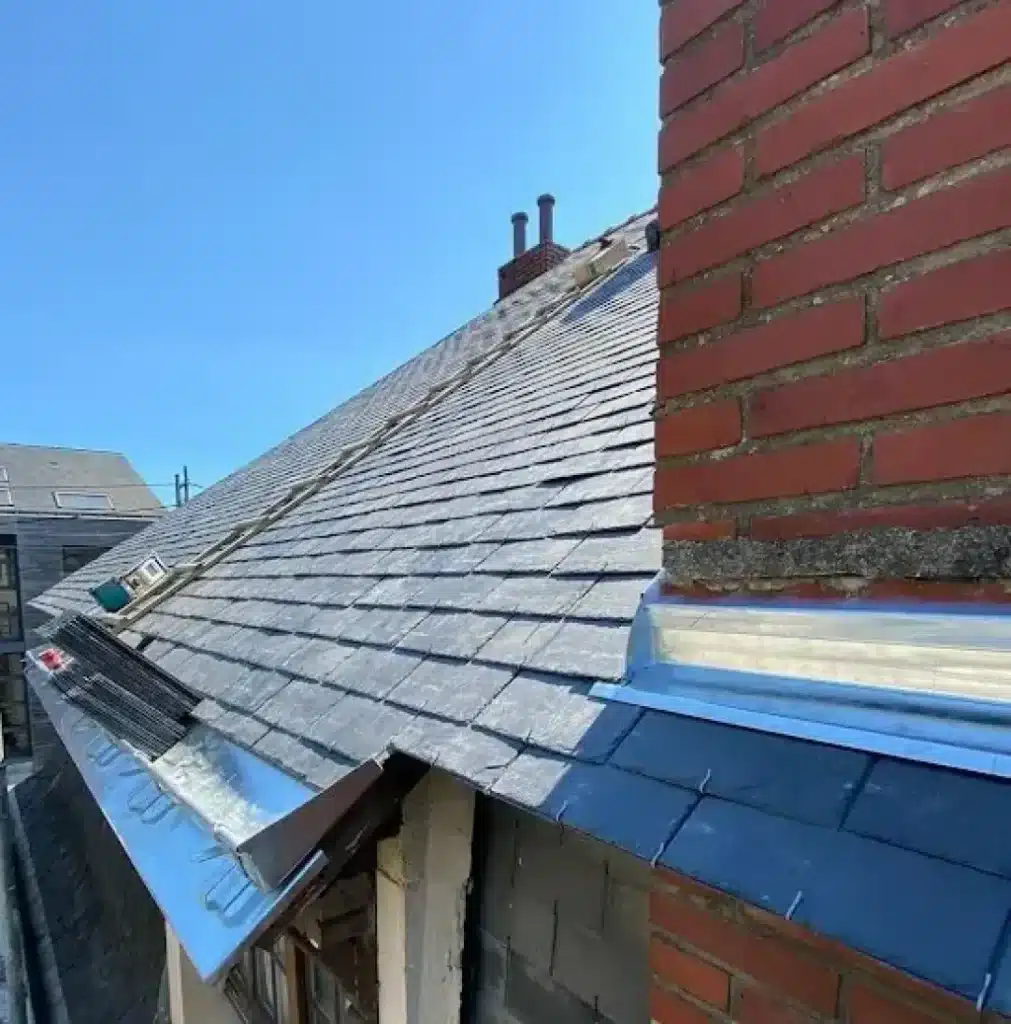 Rénovation de Toiture en Ardoise et Pose de Solin Neuf Rénovation d'une toiture en ardoise avec pose de solin de cheminée métallique et échelle de chantier.