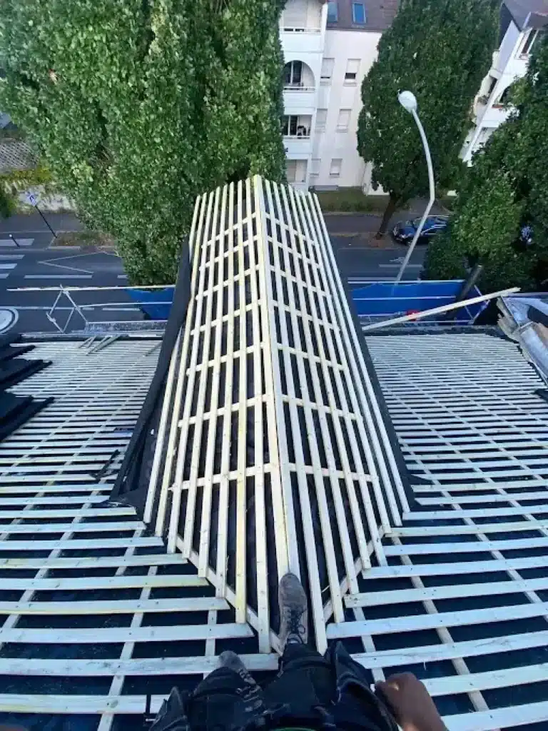 Rénovation Toiture : Installation de Charpente en Bois Vue plongeante sur la pose de liteaux en bois pour la rénovation d'une lucarne de toit par un couvreur.